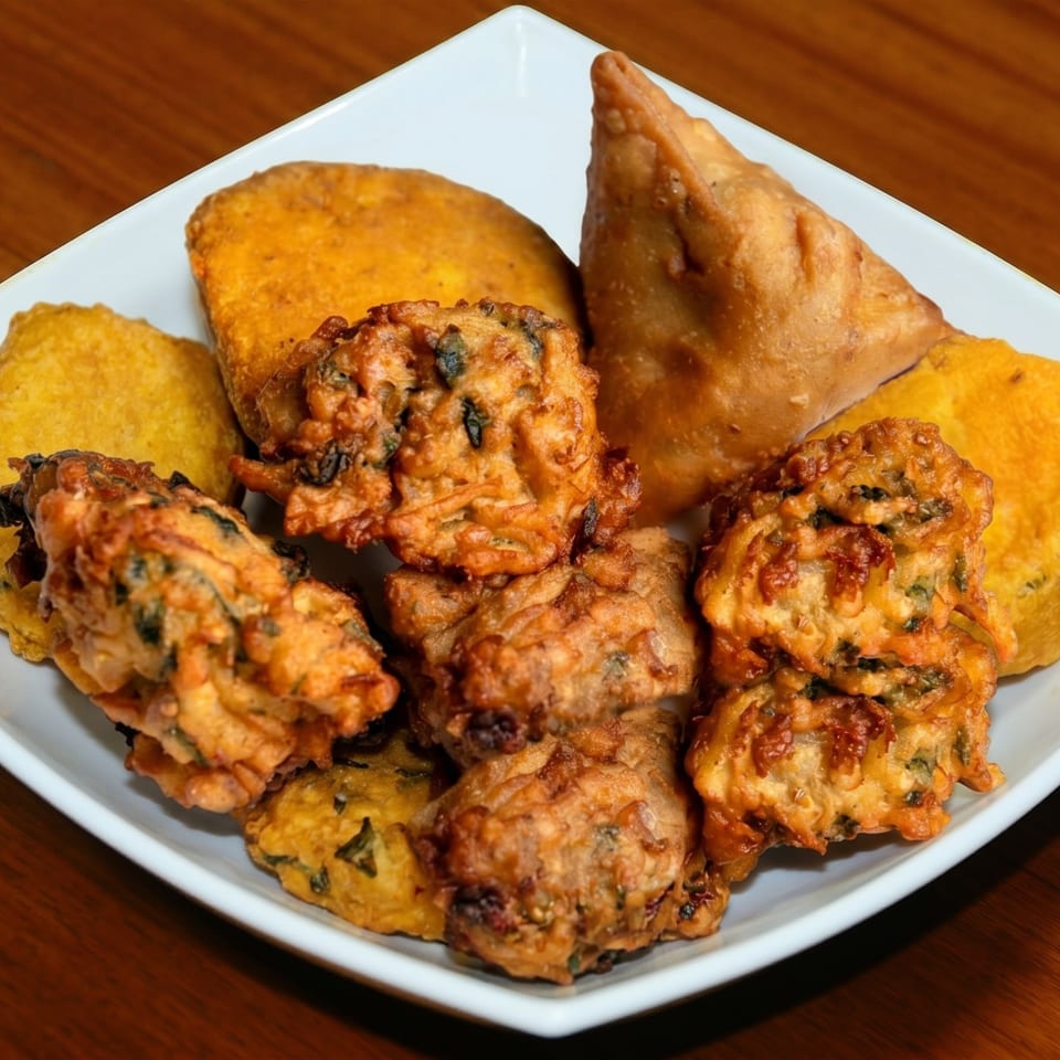 A white square plate filled with golden-brown fried Indian appetizers, including samosas and pakoras.