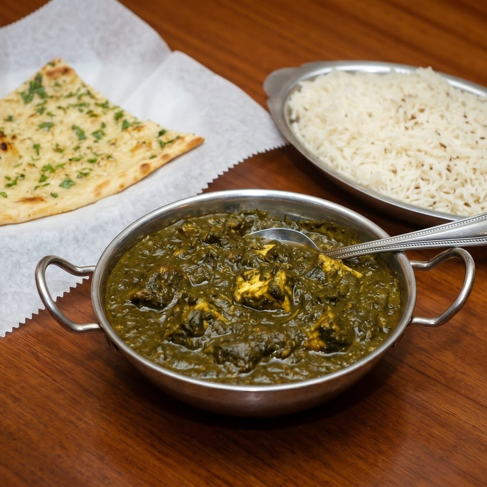 Palak paneer in a metal bowl with a spoon, naan bread, and a platter of rice.