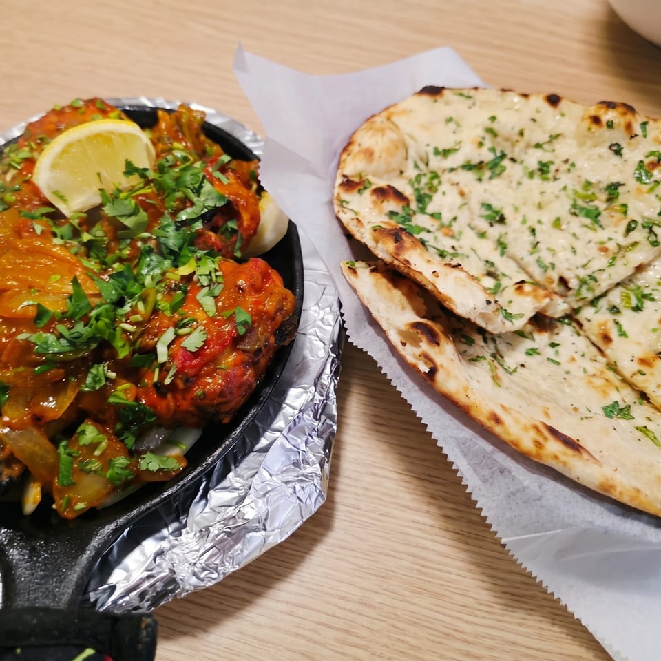 Sizzling Indian curry with lemon and cilantro in a cast iron pan, next to naan bread.