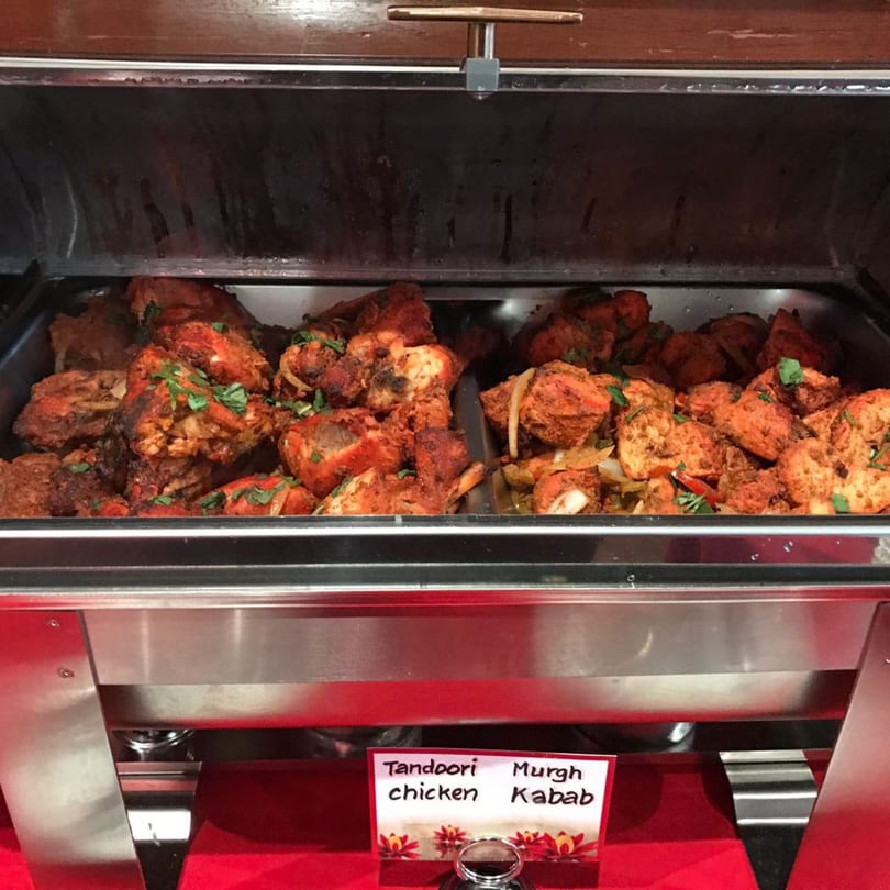 A buffet warmer filled with Tandoori chicken and Murgh Kabab, garnished with cilantro.