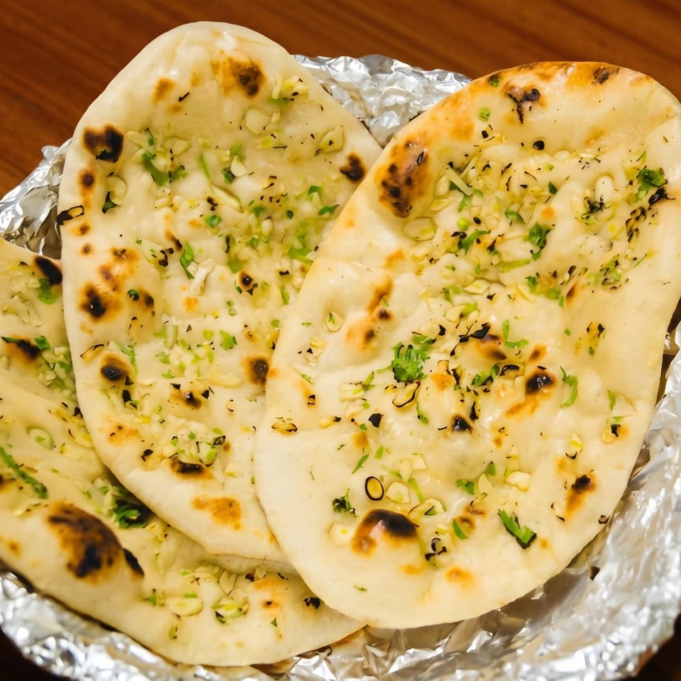 Three pieces of garlic naan bread, topped with herbs, served in aluminum foil.